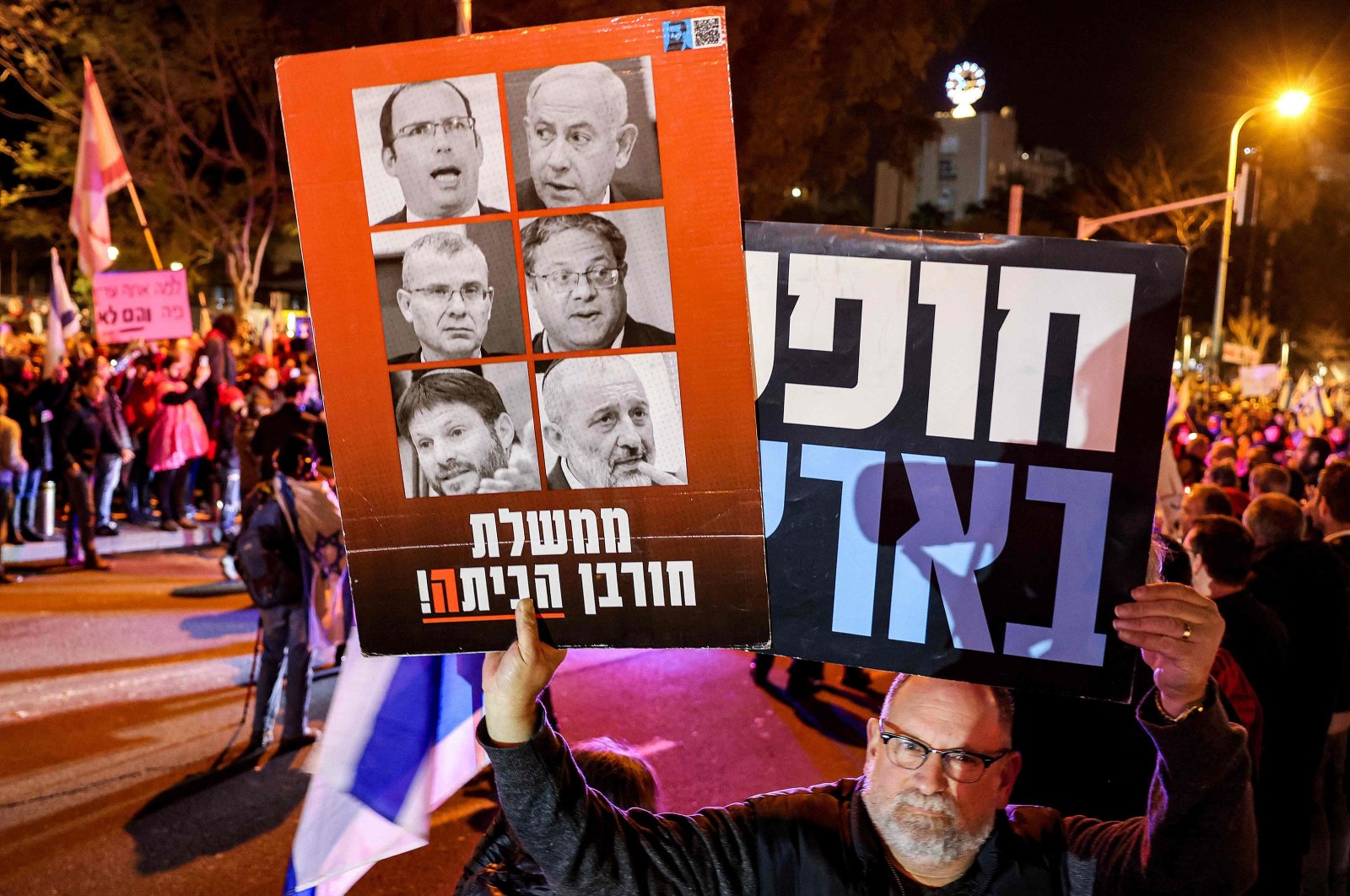 A protester holds up a sign depicting Israeli politicians: Prime Minister Benjamin Netanyahu, Justice Minister Yariv Levin, National Security Minister Itamar Ben Gvir, Finance Minister Bezalel Smotrich, and former Interior Minister Aryeh Deri with a caption reading in Hebrew "home destruction government", during an anti-government demonstration at HaBima Square in Tel Aviv on Feb. 3, 2024. (AFP Photo)