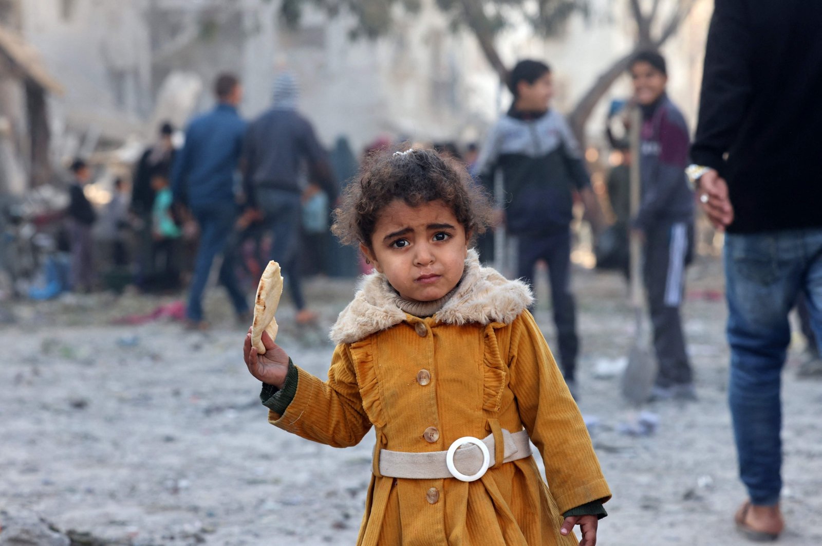 A Palestinian girl eats a piece of bread as people check debris, in Rafah, Gaza, Palestine, Feb. 22, 2024. (AFP Photo)