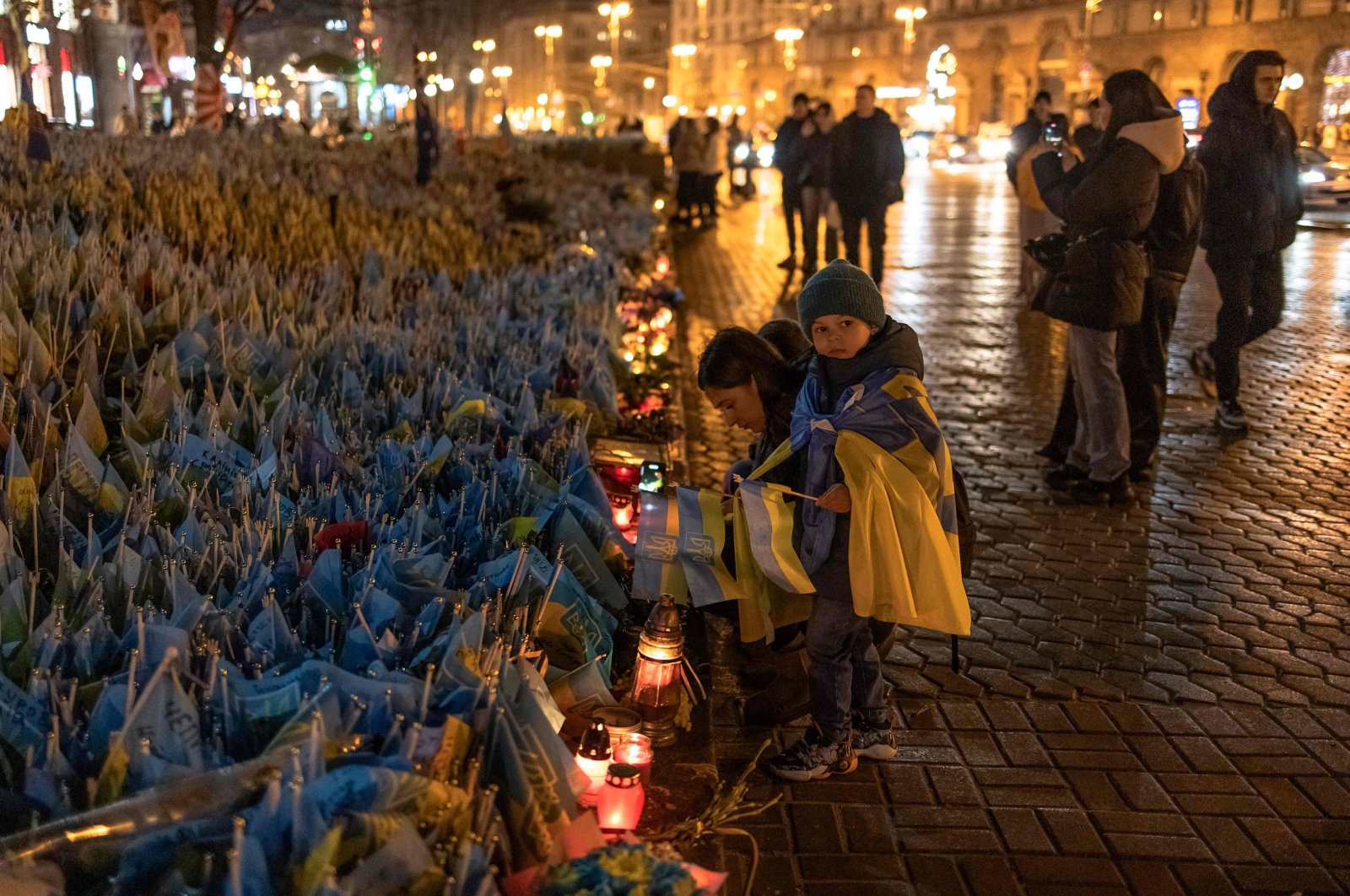 A woman and children place flags for friends in the Ukrainian military, in the area decked with flags bearing the symbols and colors of Ukraine, as the nation commemorates fallen Ukrainian army soldiers at Independence Square in Kyiv, on Feb. 24, 2024. (AFP Photo)