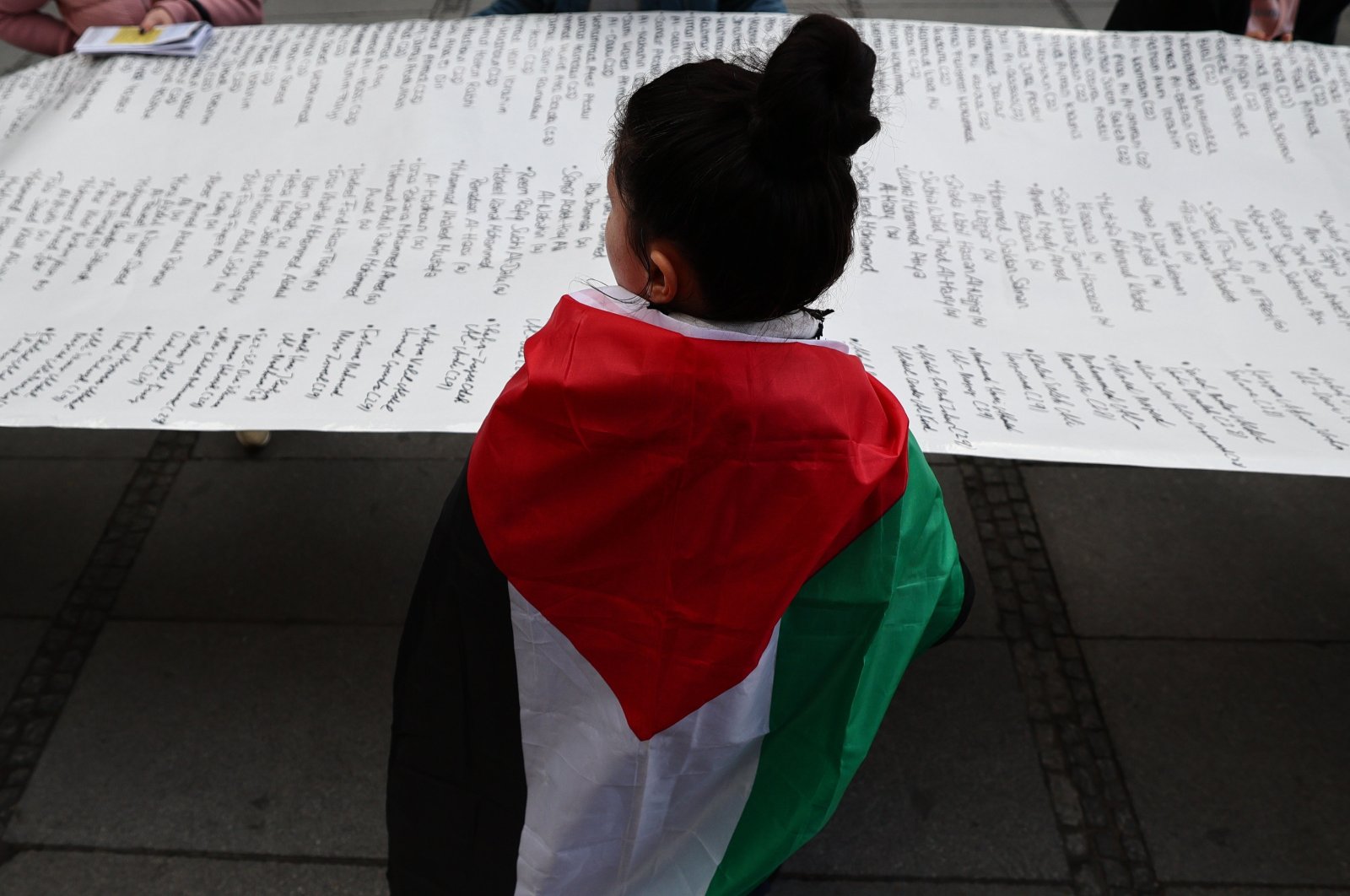 A participant covered in a Palestinian flag holds a banner summing up the victims of the Israel-Palestine conflict during a protest against the 60th Munich Security Conference (MSC) in Munich, Germany, Feb. 17, 2024. (EPA Photo)