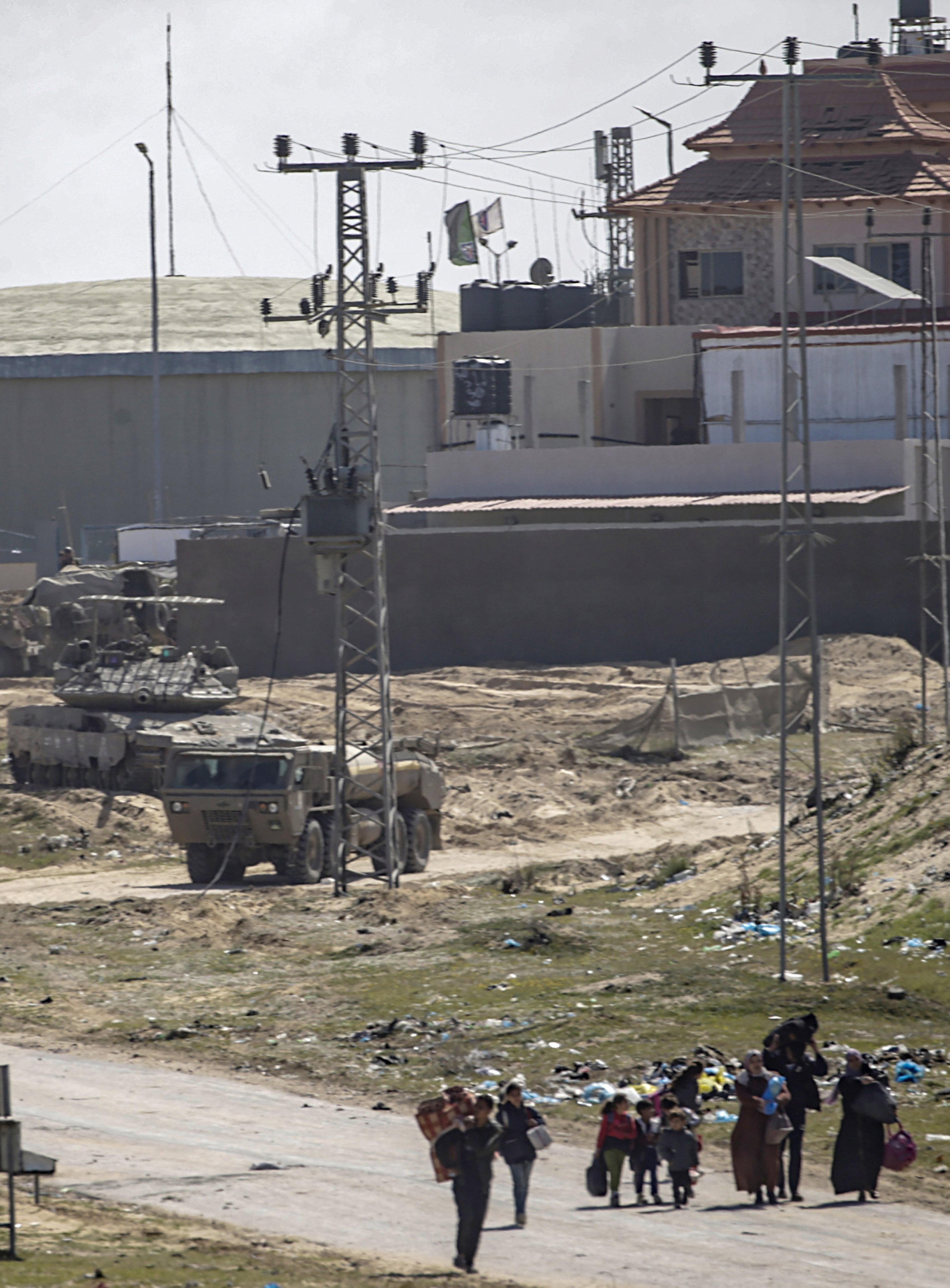 epa11198268 Israeli army vehicles on patrol (background) as internally displaced Palestinians walk after the Israeli army told residents of the Hamad area in Khan Yunis to leave their homes and head towards Rafah, near the border with Egypt, southern Gaza Strip, 04 March 2024. The Israeli military stated on 04 March that a humanitarian evacuation corridor was established to allow civilians to exit the area. More than 30,500 Palestinians and over 1,300 Israelis have been killed, according to the Palestinian Health Ministry and the Israel Defense Forces (IDF), since Hamas militants launched an attack against Israel from the Gaza Strip on 07 October 2023, and the Israeli operations in Gaza and the West Bank which followed it.  EPA/MOHAMMED SABER