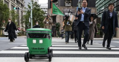 Members of the media and passersby walk next to an unmanned robot as it crosses the street during a demonstration of a robot delivery service by Uber Eats Japan, Mitsubishi Electric and robot developer Cartken in downtown Tokyo, Japan, March 5, 2024. (AFP Photo)