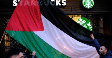 A man holds a Palestinian flag in front of a Starbucks coffee shop as people take part in a demonstration in support of Palestinians, demanding an immediate cease-fire in Gaza, Barcelona, Spain, Feb. 17, 2024. (Reuters Photo)