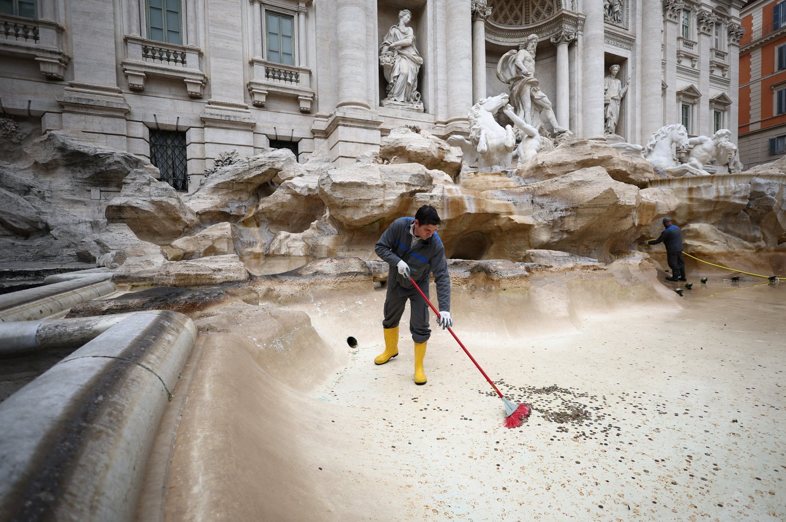 ACEA utility worker Alexio Cola uses a broom to gather coins to be collected in the emptied Trevi Fountain in Rome, Italy, Feb. 19, 2024. (Reuters Photo)