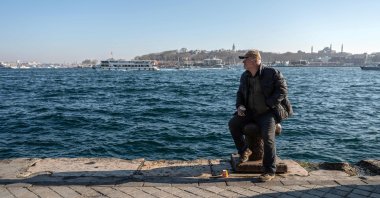 A man sits on a bollard at Karaköy district as Topkapı Palace and Hagia Sophia mosque (R) appear in the background, in Istanbul, Türkiye, Feb. 22, 2024. (AFP Photo)