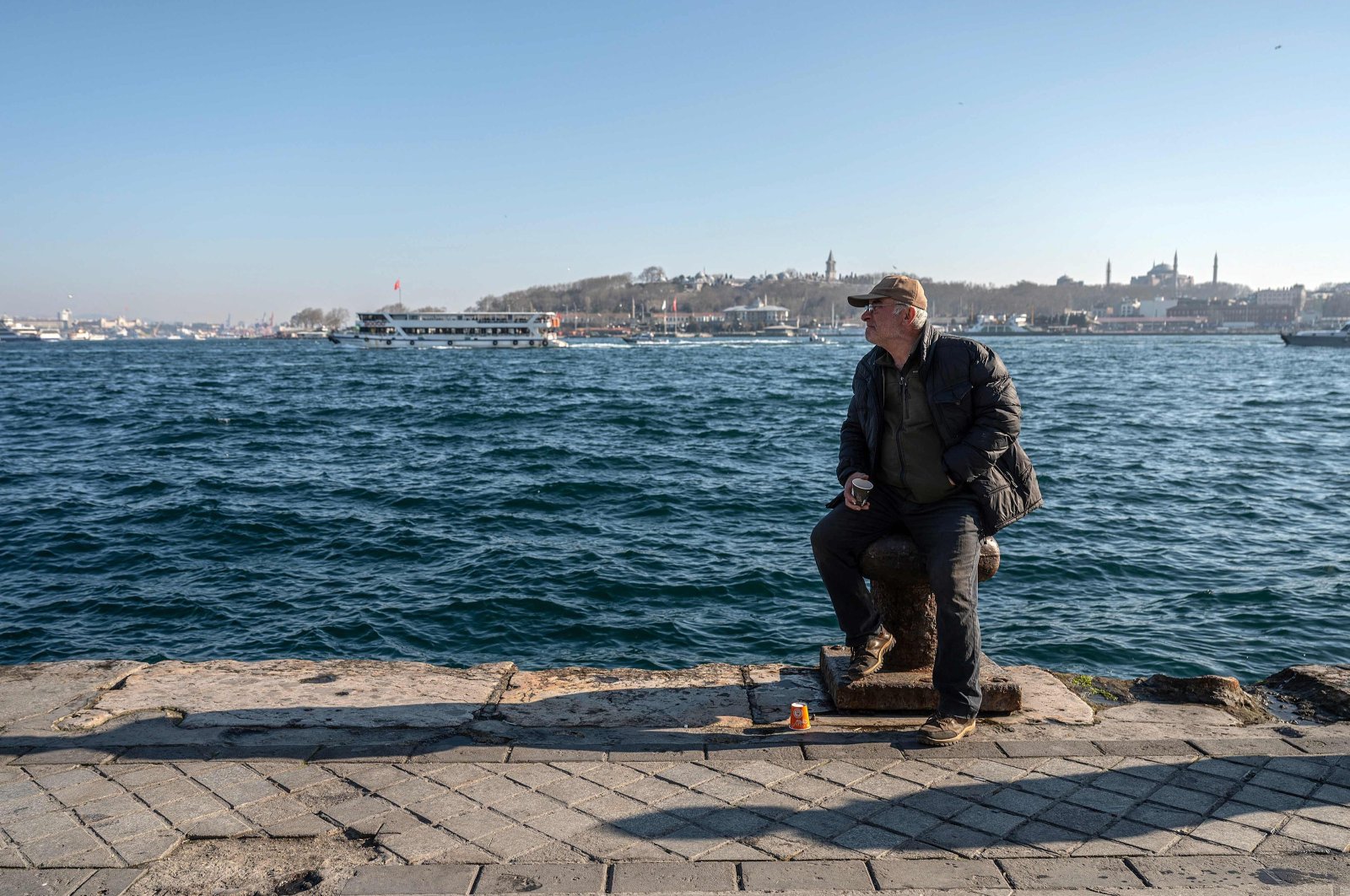 A man sits on a bollard at Karaköy district as Topkapı Palace and Hagia Sophia mosque (R) appear in the background, in Istanbul, Türkiye, Feb. 22, 2024. (AFP Photo)