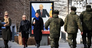 People walk in front of a poster showing Russian President Vladimir Putin and reading "The West doesn't need Russia. We need Russia!" Simferopol, occupied Crimea, Feb. 29, 2024. (AFP Photo)