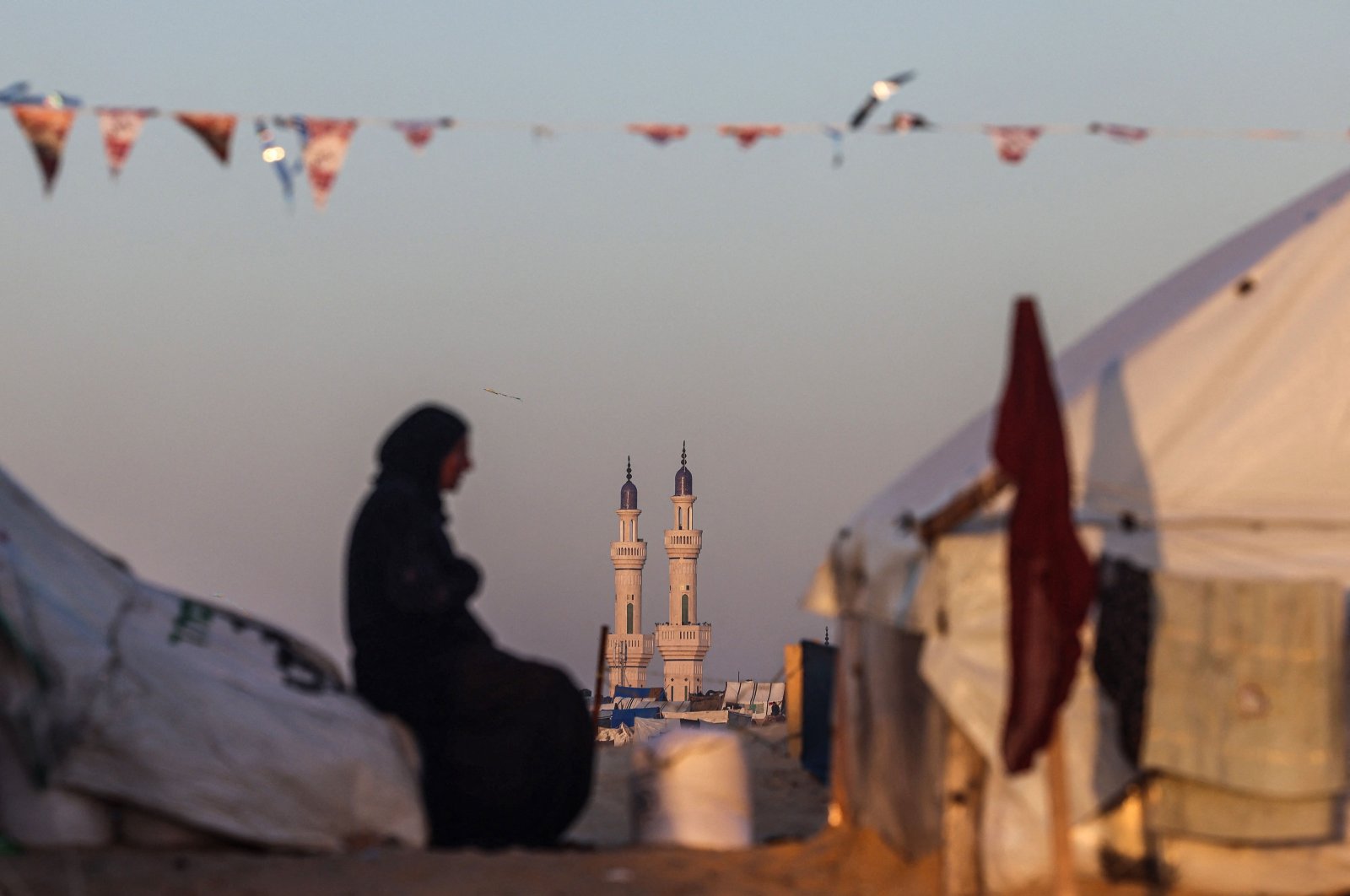 A Palestinian woman sits at a camp for displaced people backdropped by the minarets of a mosque, on the first day of the Muslim holy fasting month of Ramadan, in Rafah in the southern Gaza Strip, Palestine, March 11, 2024. (AFP Photo)