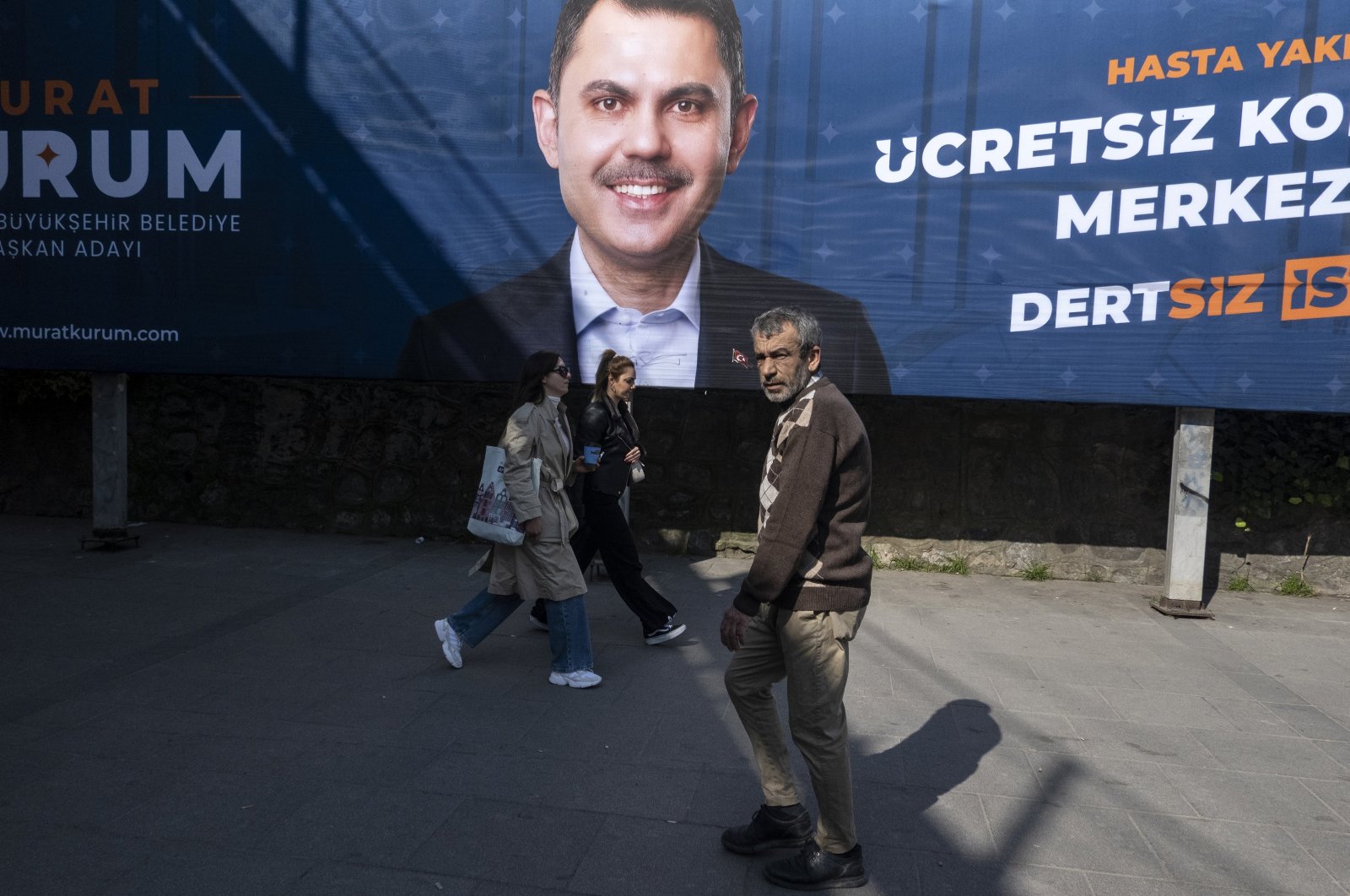 People walk in front of a local election campaign poster of Istanbul mayoral candidate Murat Kurum of the ruling AK Party (Justice and Development Party), on a street in Istanbul, Türkiye, Feb. 27, 2024. (EPA Photo)