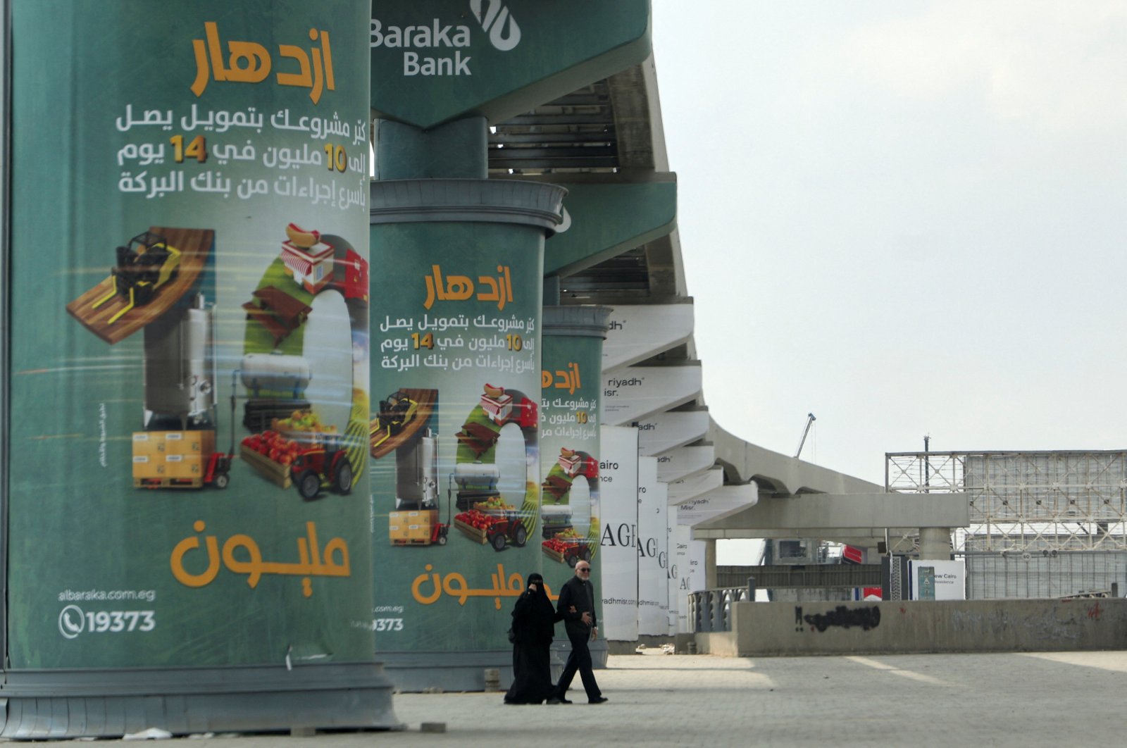 An Egyptian couple walks next to a poster advertising credit investment certificates by a branch of Al Baraka Bank on the walls of a new monorail line, Cairo, Egypt March 7, 2024. (Reuters Photo)