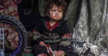 A displaced Palestinian child eats food from a box while sitting in a makeshift tent at a roadside camp, in Rafah, southern Gaza, Palestine, March 13, 2024. (AFP Photo)