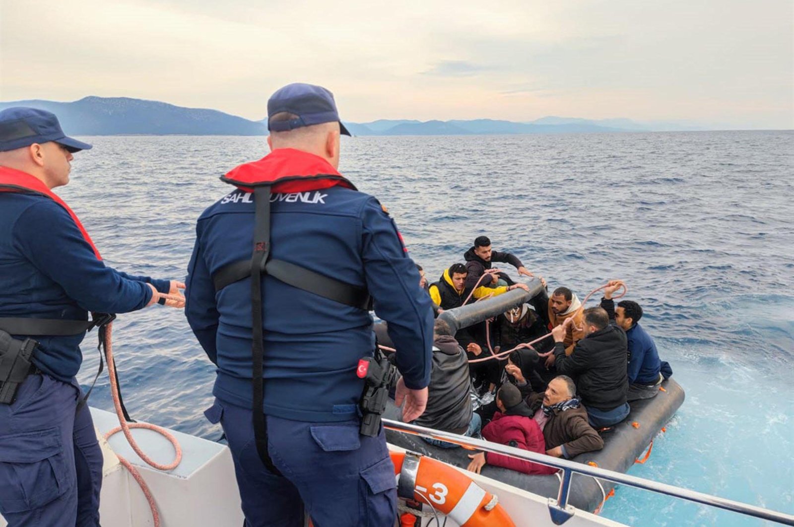Two coast guard officers pull up to a group of irregular migrants on a life raft off the coast of western Muğla province, Türkiye, March 19, 2024. (DHA Photo)