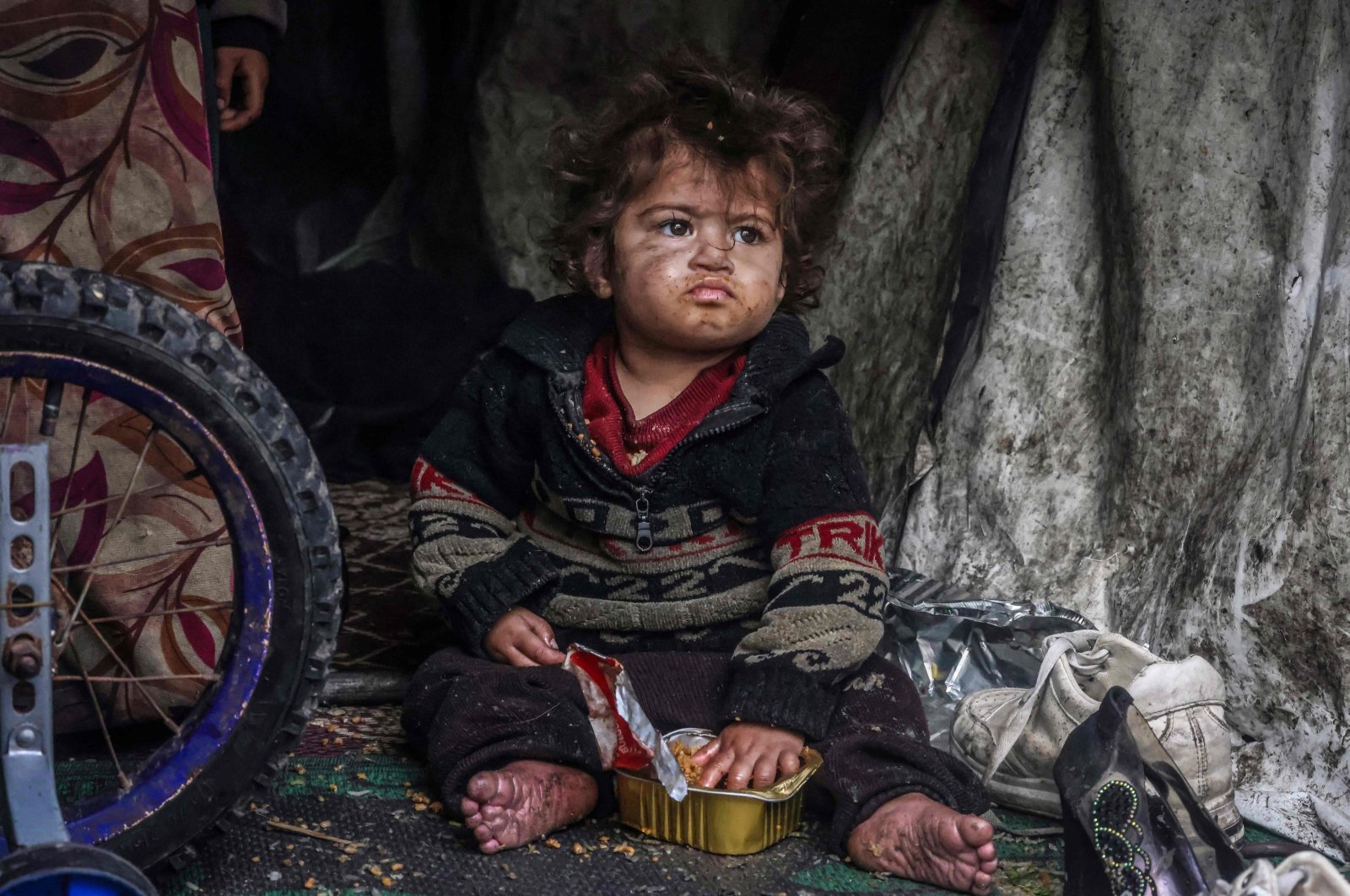 A displaced Palestinian child eats food from a box while sitting in a makeshift tent at a roadside camp, in Rafah, southern Gaza, Palestine, March 13, 2024. (AFP Photo)