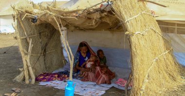 An internally displaced woman and her children sit in the shade of a straw hut at a camp in southern Gadaref state, Sudan, March 20, 2024. (AFP Photo)