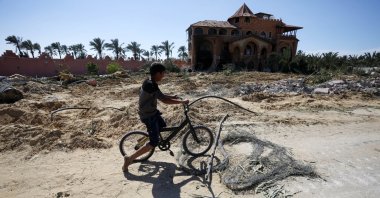A Palestinian boy rides a bike in front of a building damaged in Israeli attack on Deir al-Balah, Gaza, Palestine, March 23, 2024. (AA Photo)