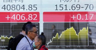 People walk past an electronic board showing a share price of the Nikkei index of the Tokyo Stock Exchange (L) and the rate of the Japanese yen versus the U.S. dollar (R) along a street, Tokyo, Japan, March 27, 2024. (AFP Photo)