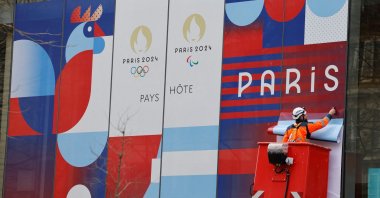 A worker sets up a giant poster announcing the Olympic Games on the facade of the Solidarity and Health Ministry, Paris, France, Feb. 27, 2024. (AFP Photo)
