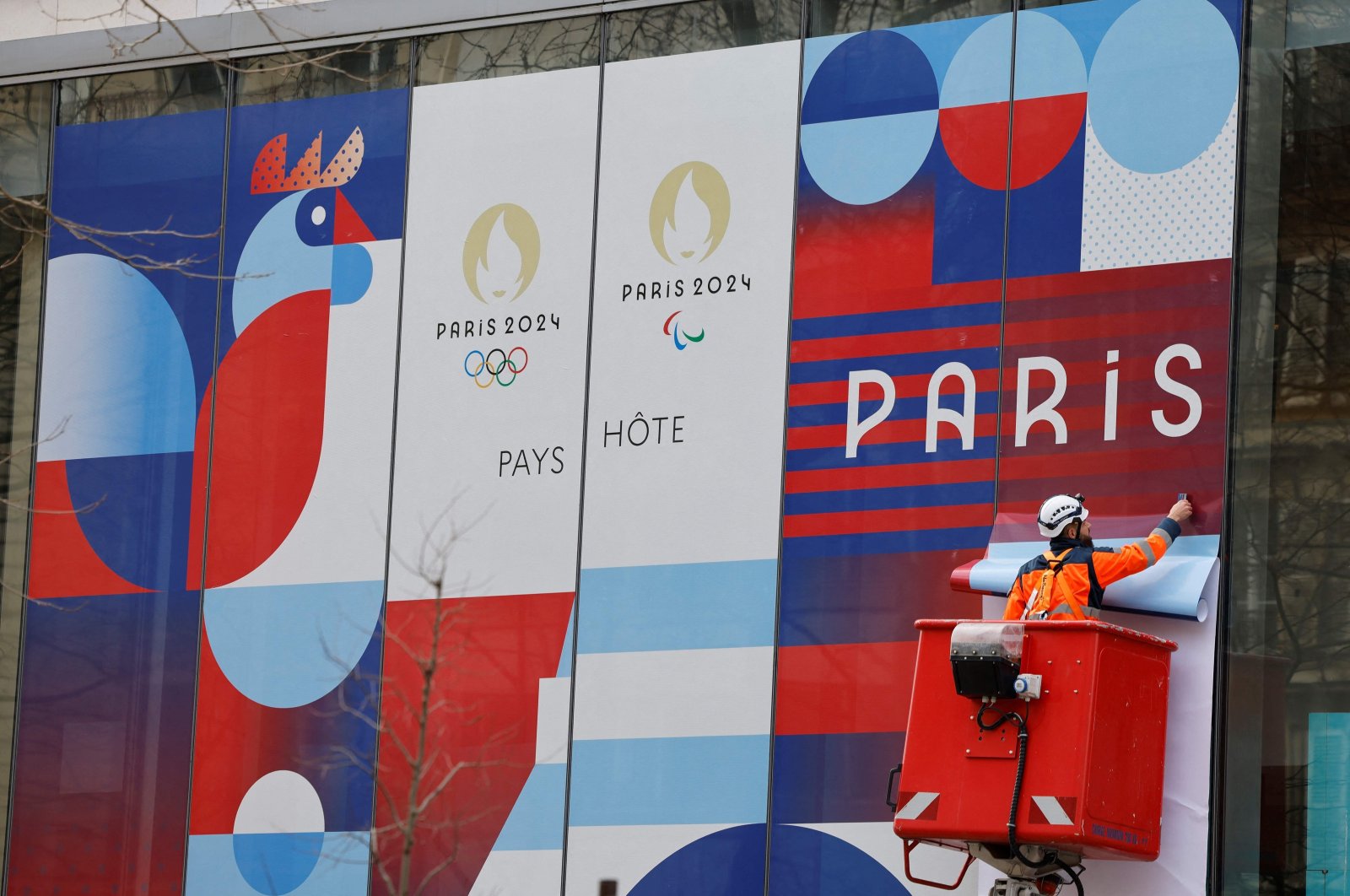 A worker sets up a giant poster announcing the Olympic Games on the facade of the Solidarity and Health Ministry, Paris, France, Feb. 27, 2024. (AFP Photo)