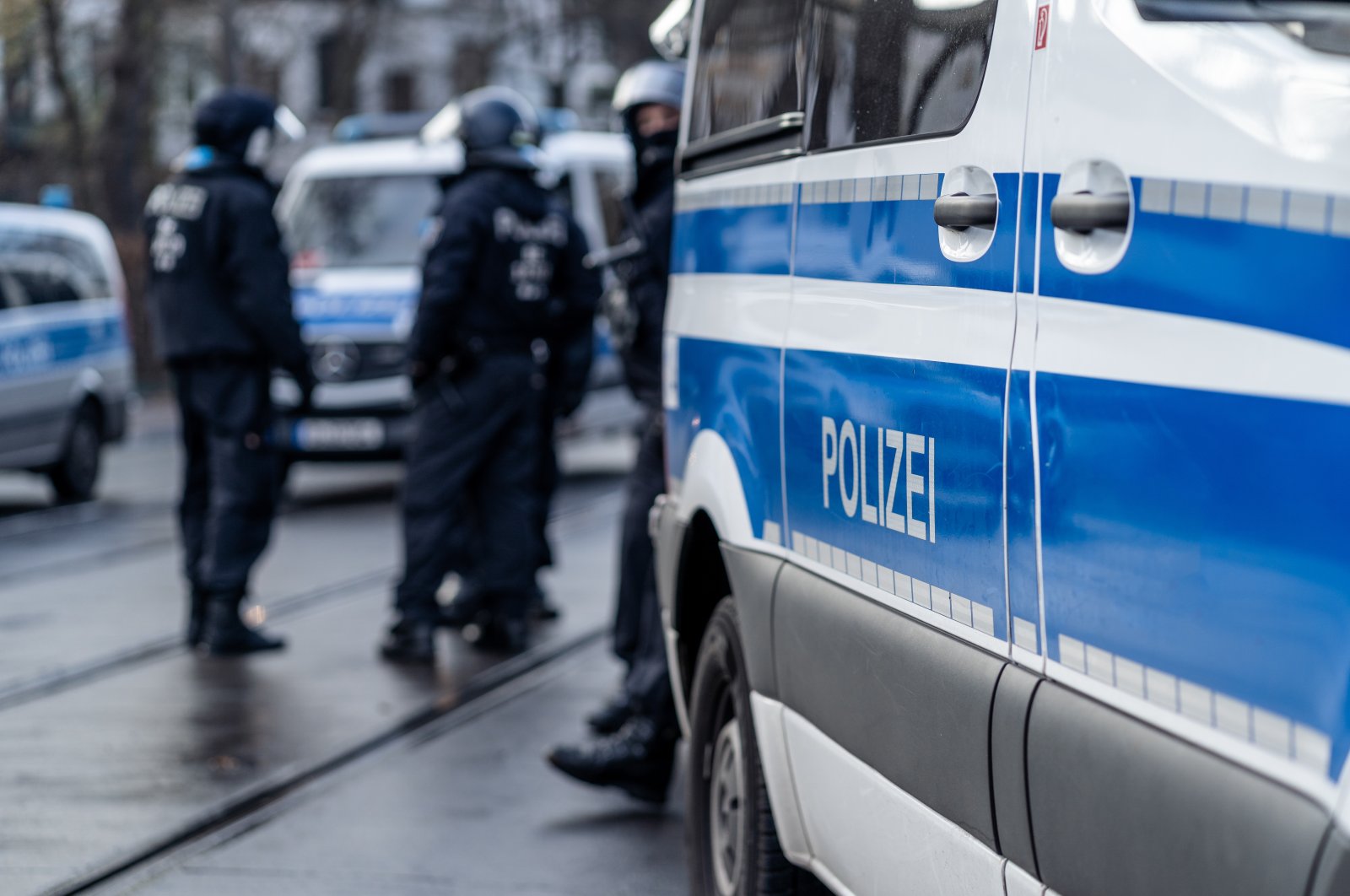 German police car from Berlin is in the focus and in the blurry background are several riot police cops standing on the street and waiting for action on a demonstration, Dec. 13, 2020. (Shutterstock File Photo)