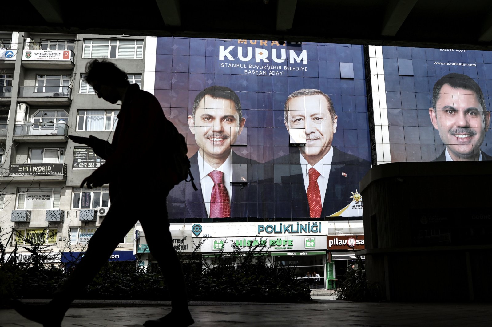 A person walks past images of President Recep Tayyip Erdoğan (C) and Justice and Development Party&#039;s (AK) Istanbul mayoral candidate Murat Kurum (L, R) as part of the campaign for the upcoming local elections in Istanbul, Türkiye, March 27, 2024. (EPA Photo)