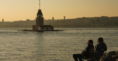 People sit near the Maiden&#039;s Tower as the sun sets at the Bosporus, in Istanbul, Türkiye, March 23, 2024. (AP Photo)
