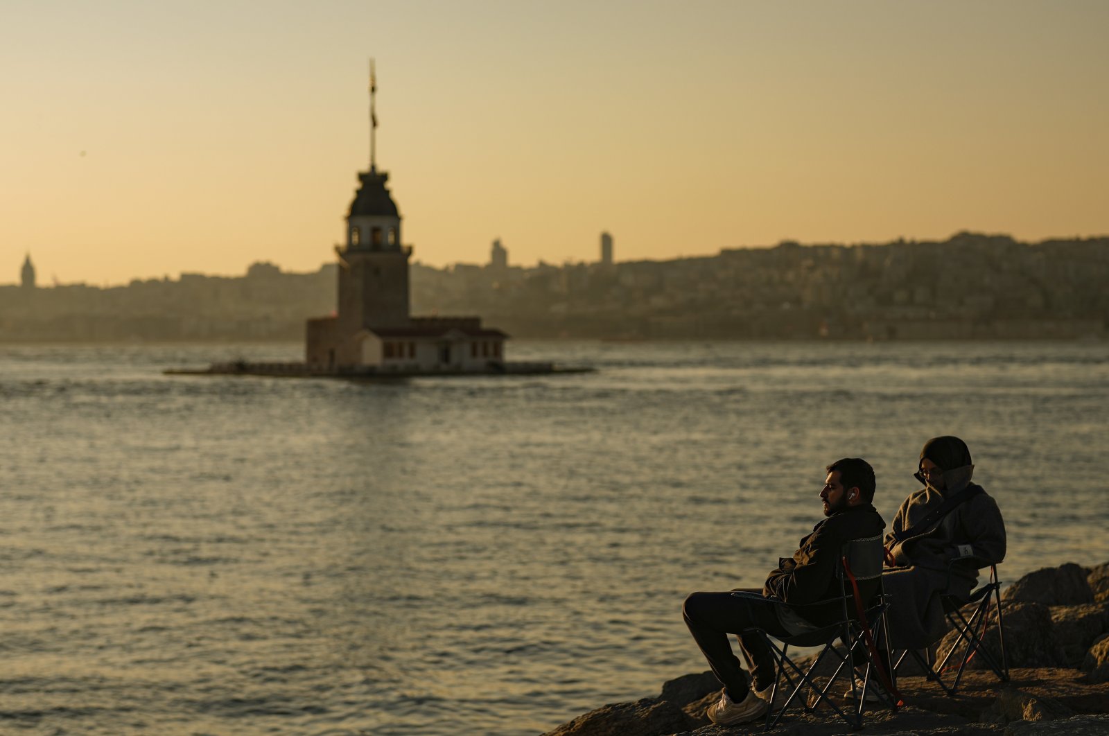 People sit near the Maiden&#039;s Tower as the sun sets at the Bosporus, in Istanbul, Türkiye, March 23, 2024. (AP Photo)