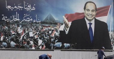 Workers clean the street under a billboard supporting Egyptian President Abdel-Fattah el-Sissi, in Cairo, Egypt, Dec. 10, 2023. (AP Photo)