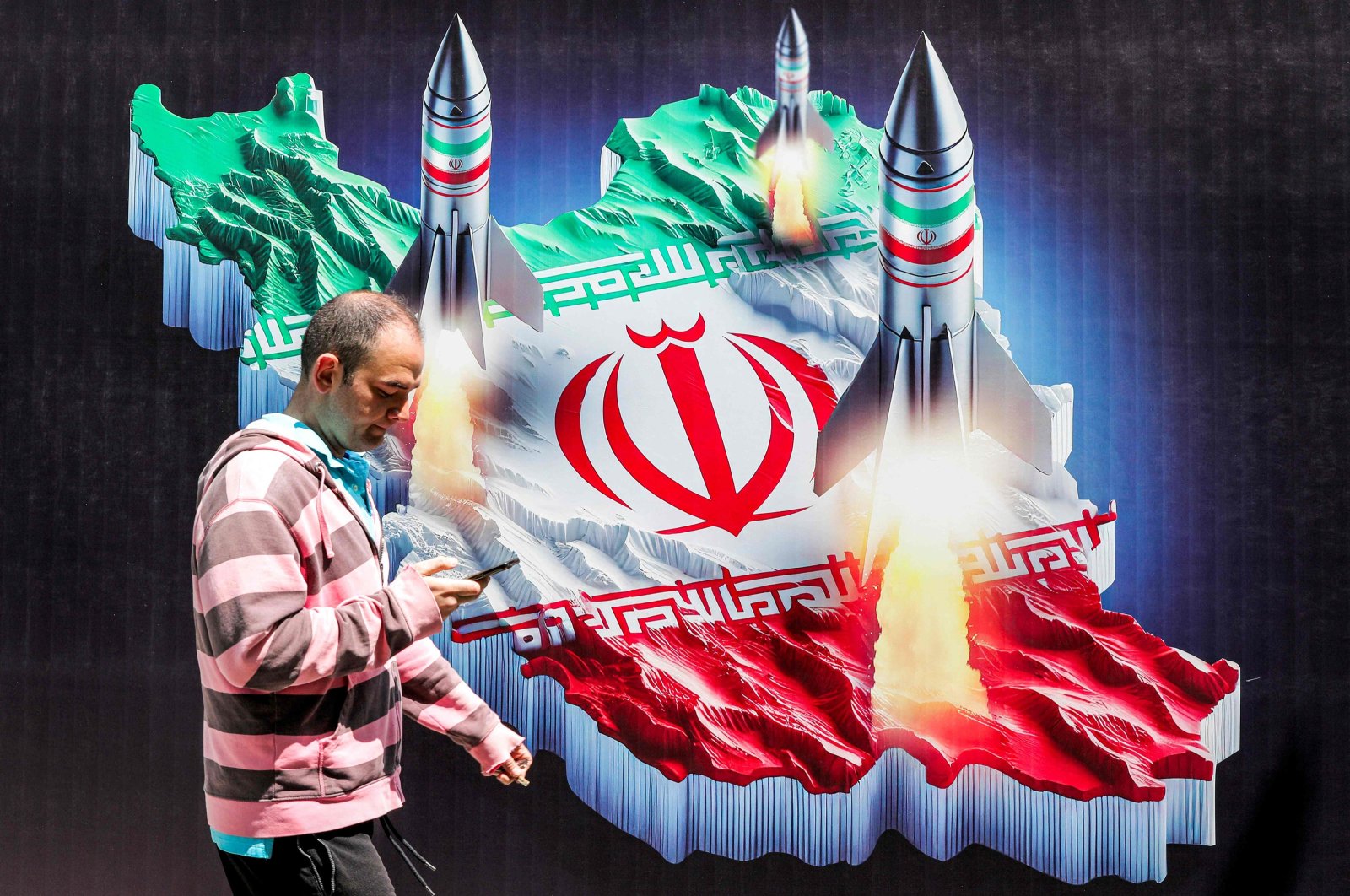 A man walks past a banner depicting missiles launching from a representation of the map of Iran colored with the Iranian flag, Tehran, Iran, April 15, 2024. (AFP Photo)