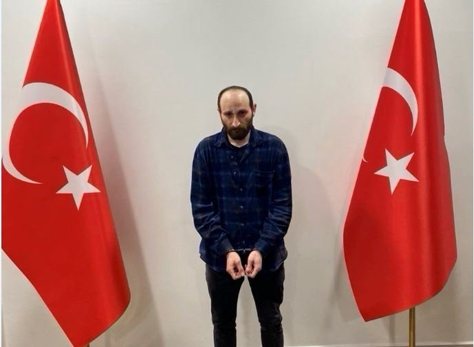 The handcuffed suspect stands between Turkish flags in this photo distributed by Turkish authorities to the media on April 18, 2024. (DHA Photo)