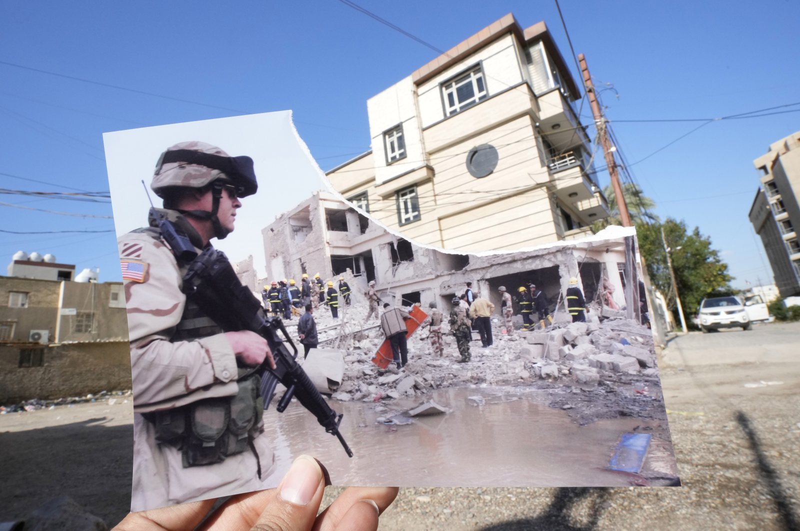 A photograph of a US soldier securing the area near a destroyed building after two car bombs detonated in a central Baghdad residential neighborhood on Nov. 18, 2005, killing at least six people and wounding dozens, is inserted into the scene at the same location, 20 years after the U.S. led invasion on Iraq and subsequent war, Baghdad, Iraq, March 10, 2023. (AP Photo)