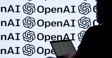 A person is photographed using a device with the backdrop of the OpenAI logo, April 22, 2024. (AA Photo)