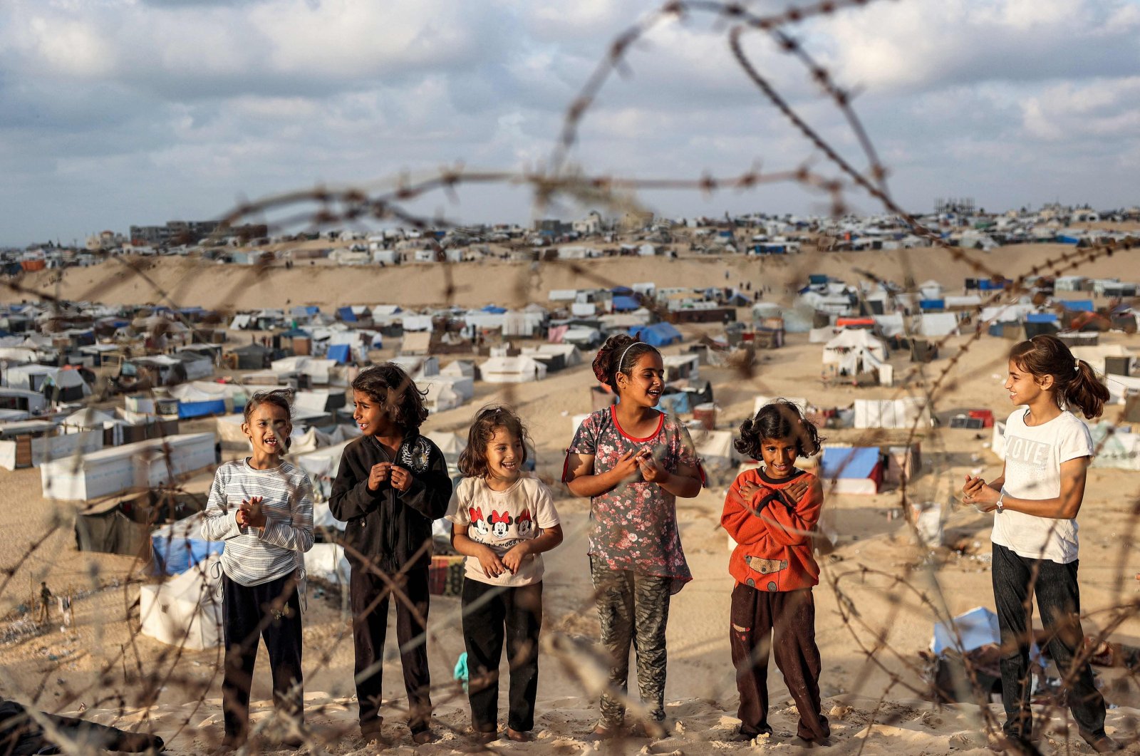 Children stand behind barbed wire along a slope near a camp housing displaced Palestinians in Rafah in the southern Gaza Strip, April 30, 2024. (AFP Photo)
