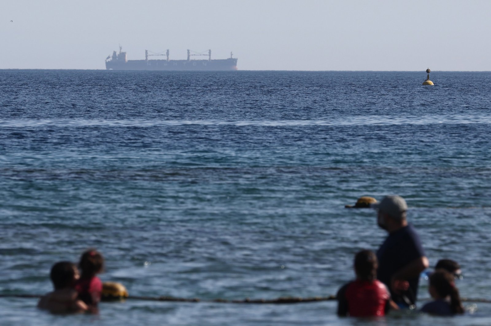 People enjoy the beach as a cargo ship sails in the background, near the Red Sea port of Eilat, southern Israel, April 16, 2024. (EPA Photo)
