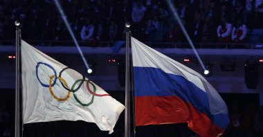 The Russian national flag (R) flies after it is hoisted next to the Olympic flag during the closing ceremony of the 2014 Winter Olympics, Sochi, Russia, Feb. 23, 2014. (AP Photo)