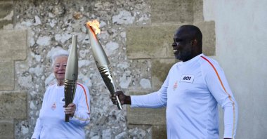 French former football player Basile Boli (R) holds the Olympic Torch and lights up the torch of French founder of Olympique de Marseille supporters club "Dodger&#039;s Marseille" Colette Cataldo as part of the Olympic and Paralympic Torch Relays at the Basilica of Notre Dame de la Garde, ahead of the Paris 2024 Olympic and Paralympic Games, Marseille, France, May 9, 2024. (AFP Photo)