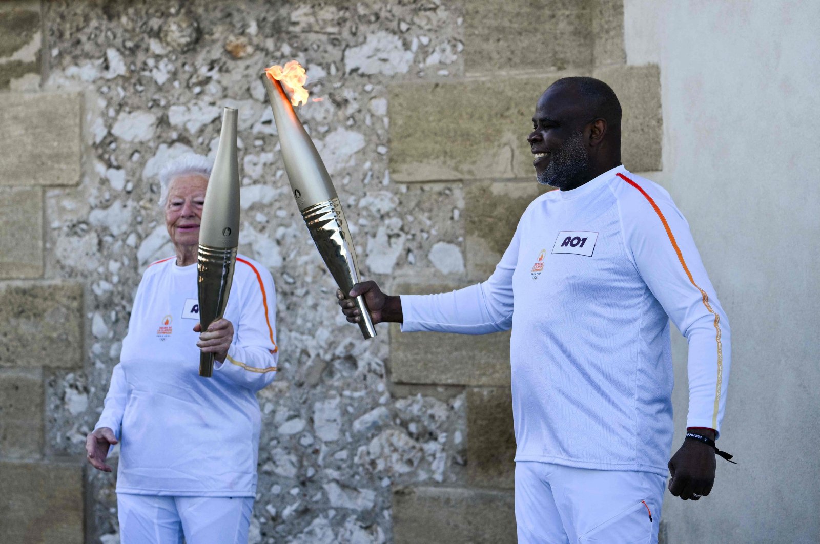 French former football player Basile Boli (R) holds the Olympic Torch and lights up the torch of French founder of Olympique de Marseille supporters club "Dodger&#039;s Marseille" Colette Cataldo as part of the Olympic and Paralympic Torch Relays at the Basilica of Notre Dame de la Garde, ahead of the Paris 2024 Olympic and Paralympic Games, Marseille, France, May 9, 2024. (AFP Photo)