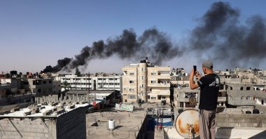 A man snaps pictures from a rooftop as thick, black smoke rises from a fire in a building caused by Israeli bombardment in Rafah in the southern Gaza Strip, Palestine, May 10, 2024. (AFP Photo)