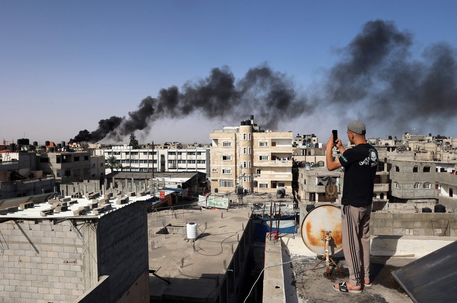 A man snaps pictures from a rooftop as thick, black smoke rises from a fire in a building caused by Israeli bombardment in Rafah in the southern Gaza Strip, Palestine, May 10, 2024. (AFP Photo)