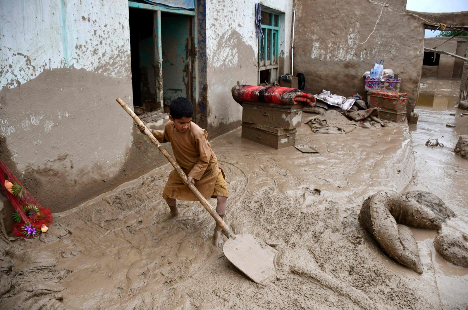 An Afghan boy shovels mud from the courtyard of a house following flash floods at a village in Baghlan-e-Markazi district of Baghlan province, Afghanistan, May 11, 2024.