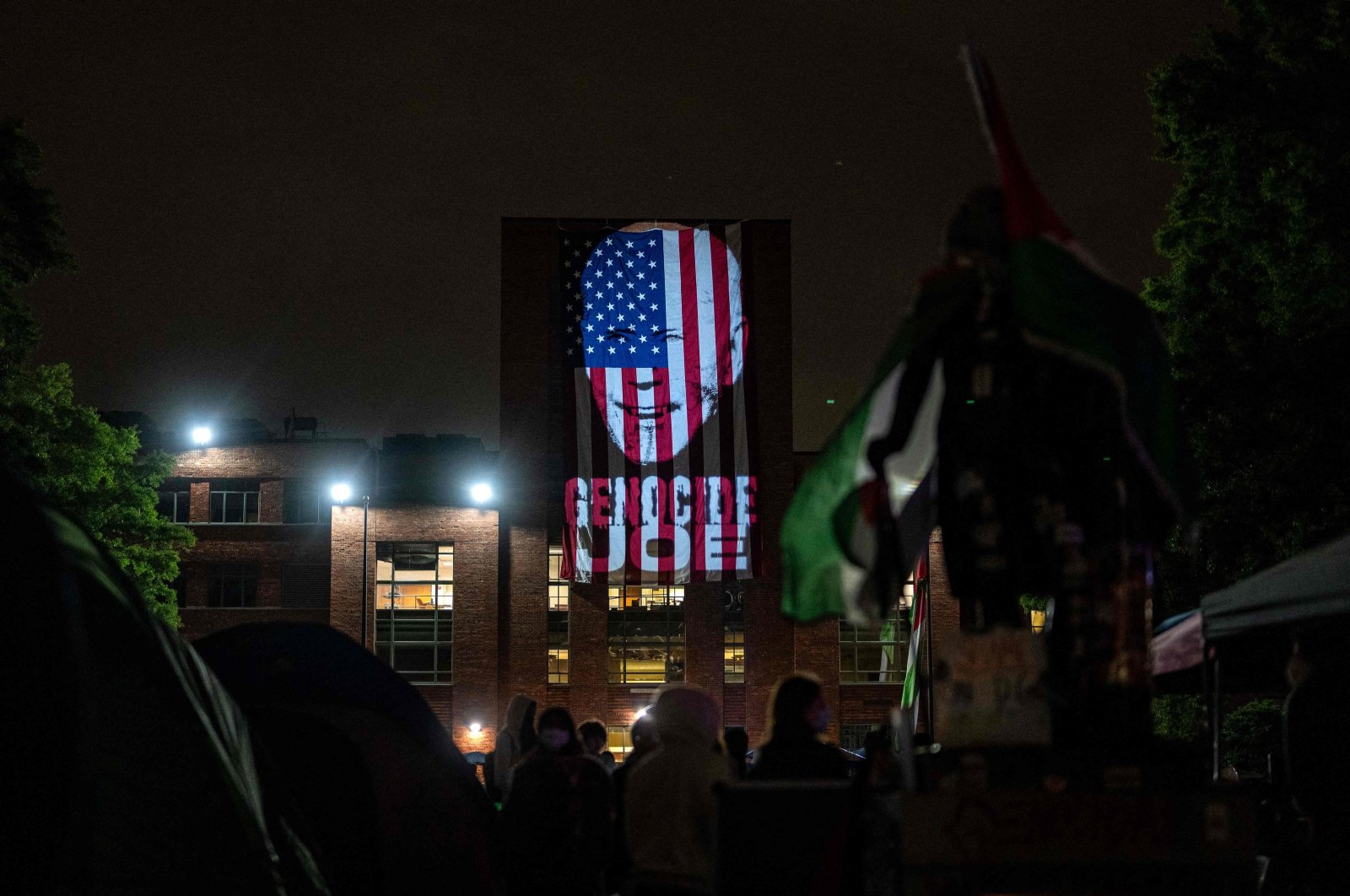  An image of President Joe Biden with the words &quot;Genocide Joe&quot; is projected on an American flag that hangs from GWU Law School&#039;s Lisner Hall at an encampment at University Yard at George Washington University on May 3, 2024 in Washington, D.C. (Getty Images via AFP)