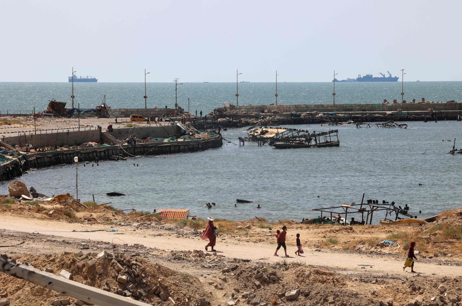 Palestinians walk past a jetty in Gaza City with a view of navy vessels off the coast as part of a humanitarian &quot;maritime corridor&quot; announced by U.S. Central Command (CENTCOM) May 17, 2024. (AFP Photo)
