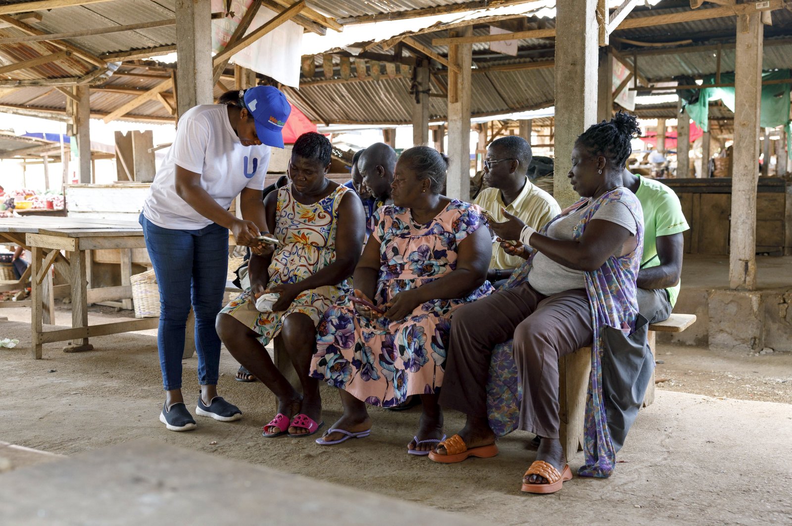 Rita Quansah (L) from Uniti Networks, coaches farmers on how to navigate its platform of applications at a market in Hohoe, Ghana, April 18, 2024. (AP Photo)