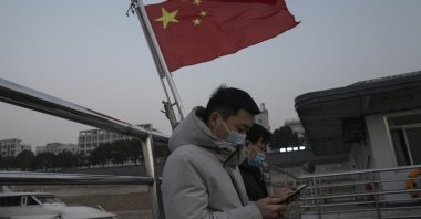 Residents taking the ferry stand near a Chinese national flag in Wuhan, in central China&#039;s Hubei province, Jan. 15, 2021. (AP Photo)