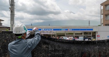 A worker installing a barrier to block the sight of Japan&#039;s Mount Fuji emerging from behind a convenience store to deter badly behaved tourists in the town of Fujikawaguchiko, Japan, May 21, 2024. (AFP File Photo)