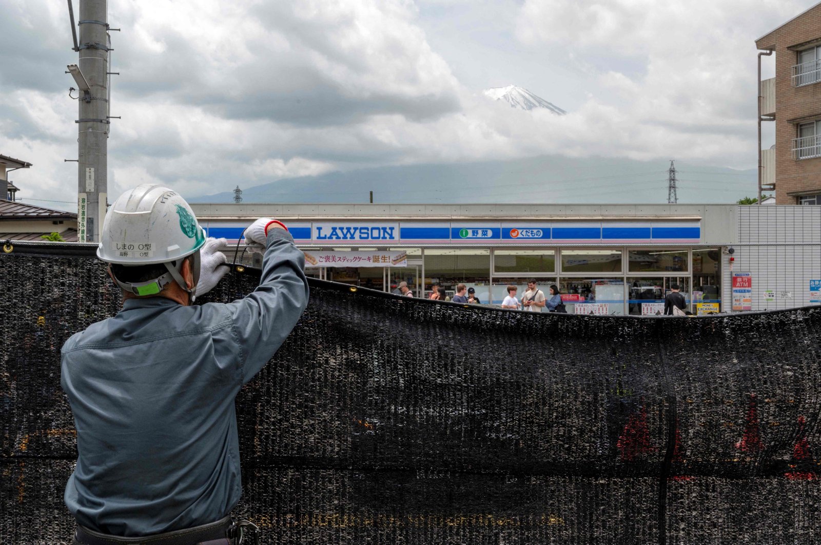 A worker installing a barrier to block the sight of Japan&#039;s Mount Fuji emerging from behind a convenience store to deter badly behaved tourists in the town of Fujikawaguchiko, Japan, May 21, 2024. (AFP File Photo)