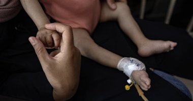 Palestinian child Yousef al-Jojo sits on his mother's lap as she holds his hand at Al-Aqsa Martyrs Hospital in Deir al-Balah, Gaza Strip, June 1, 2024. (EPA Photo)