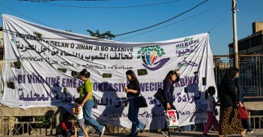 Syrian Kurdish women walk past a campaign banner for the PKK/YPG&#039;s so-called elections in the northeastern city of Qamishli, Syria, June 6, 2024. (AFP Photo)