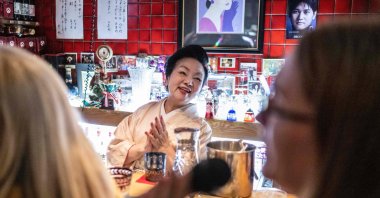 &quot;Mama-san&quot; Kuri Awaji (C), who runs a snack bar, claps her hands as a tourist from the U.S. (R) on a snack bar tour sings karaoke at the bar &quot;Kuriyakko,&quot; Tokyo, Japan, March 22, 2024. (AFP Photo)