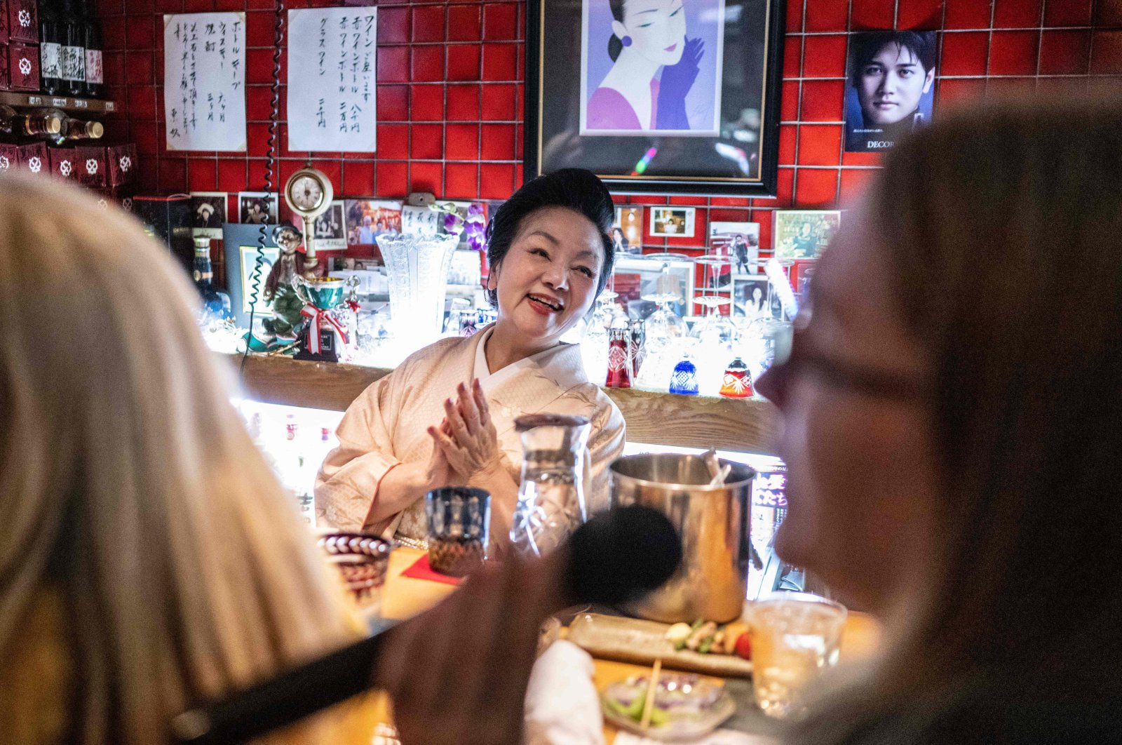 &quot;Mama-san&quot; Kuri Awaji (C), who runs a snack bar, claps her hands as a tourist from the U.S. (R) on a snack bar tour sings karaoke at the bar &quot;Kuriyakko,&quot; Tokyo, Japan, March 22, 2024. (AFP Photo)