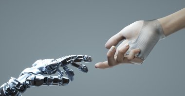 Digital generated image of female hand touching robotic hand against grey background. (Getty Images Illustration)